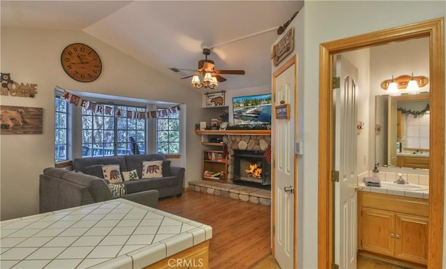 living room with lofted ceiling, a stone fireplace, sink, light hardwood / wood-style flooring, and ceiling fan