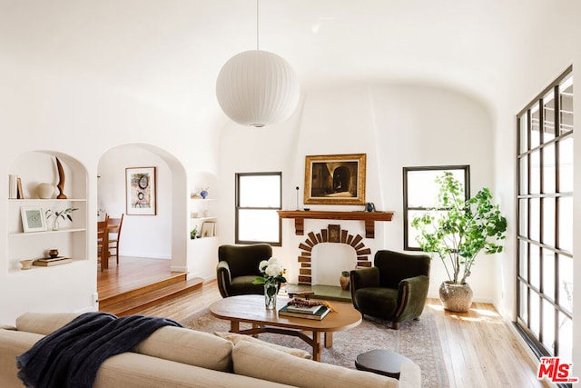 living room with a large fireplace, light wood-type flooring, and a towering ceiling