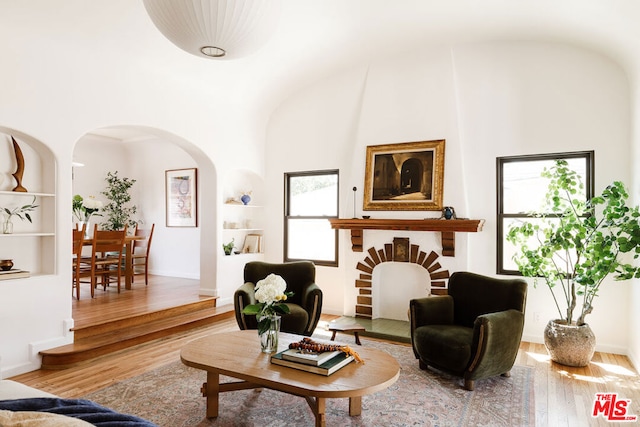 living room featuring wood-type flooring, built in features, and a high ceiling