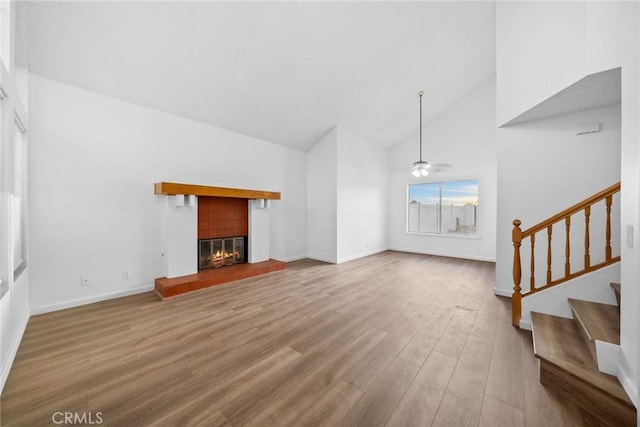 unfurnished living room with a tiled fireplace, ceiling fan, high vaulted ceiling, and wood-type flooring