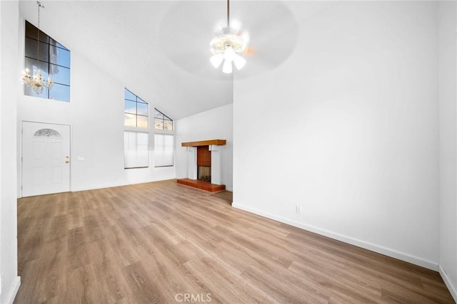 unfurnished living room featuring high vaulted ceiling, light hardwood / wood-style floors, and ceiling fan with notable chandelier