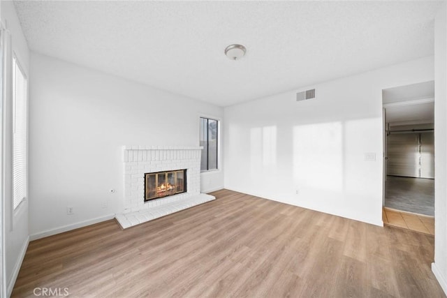 unfurnished living room featuring light wood-type flooring, a textured ceiling, and a brick fireplace