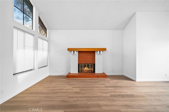 unfurnished living room featuring a towering ceiling, a textured ceiling, a tile fireplace, and light hardwood / wood-style flooring