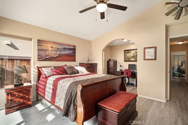 bedroom featuring baseboards, vaulted ceiling, wood finished floors, arched walkways, and a textured ceiling