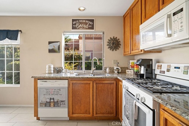 kitchen with baseboards, light stone countertops, brown cabinets, white appliances, and a sink