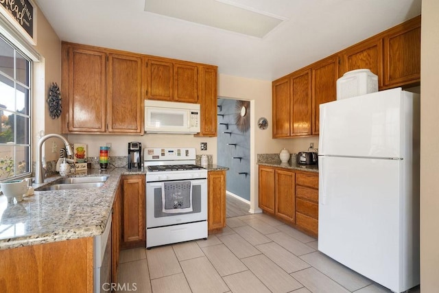 kitchen featuring brown cabinetry, white appliances, light stone counters, and a sink