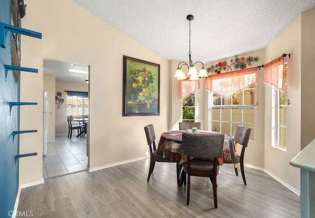 dining area with a chandelier, vaulted ceiling, a textured ceiling, and wood finished floors