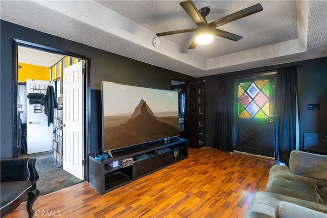 cinema with hardwood / wood-style floors, ceiling fan, a raised ceiling, and a textured ceiling