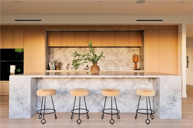 bar with black double oven, backsplash, and light hardwood / wood-style floors