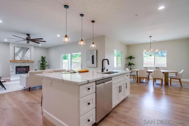 kitchen featuring stainless steel dishwasher, ceiling fan with notable chandelier, decorative light fixtures, a center island with sink, and white cabinets