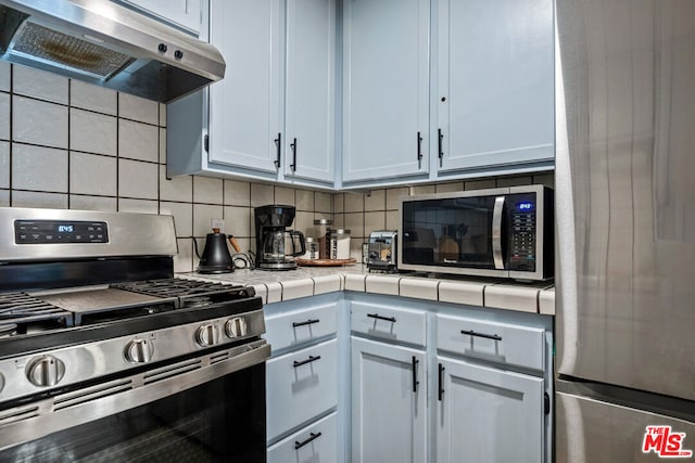 kitchen featuring white cabinets, stainless steel appliances, tile countertops, and exhaust hood