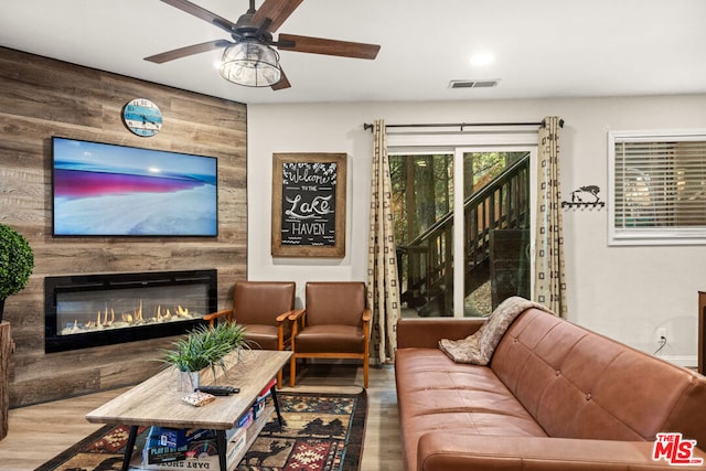 living room featuring wood walls, ceiling fan, a large fireplace, and wood-type flooring