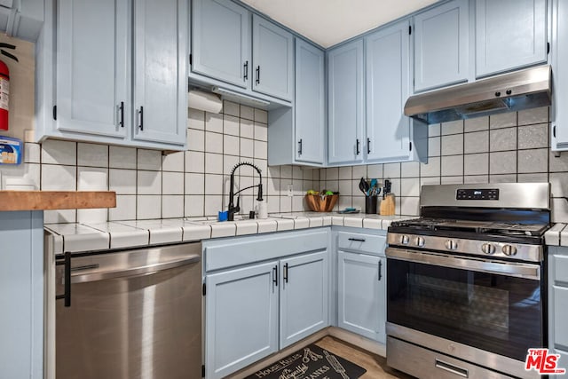 kitchen featuring tasteful backsplash, stainless steel appliances, sink, light hardwood / wood-style flooring, and tile counters