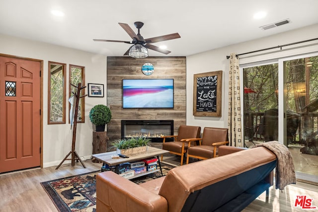 living room featuring ceiling fan, a large fireplace, and light hardwood / wood-style flooring