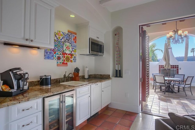 kitchen with wine cooler, white cabinetry, sink, and stone countertops