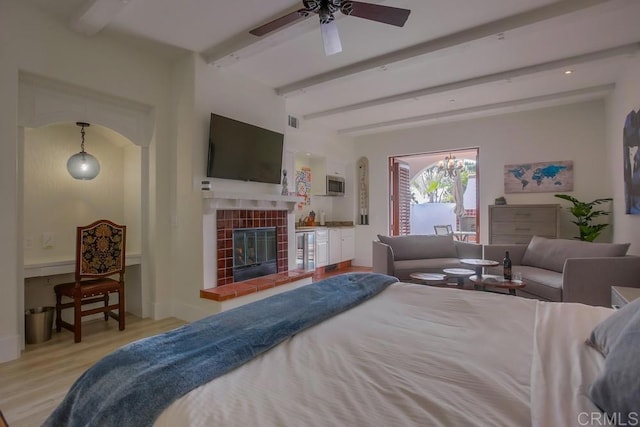 bedroom with beamed ceiling, ceiling fan, light hardwood / wood-style floors, and a tiled fireplace