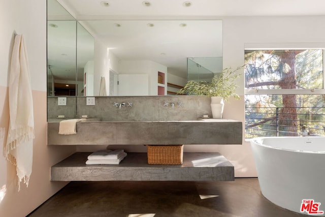 bathroom with concrete flooring, a tub to relax in, tasteful backsplash, and plenty of natural light