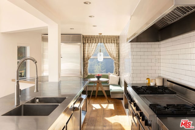 kitchen featuring sink, wall chimney exhaust hood, backsplash, wood-type flooring, and stainless steel stove