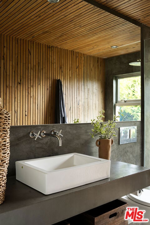 bathroom featuring wood walls, wood ceiling, and sink