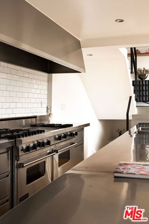 kitchen featuring double oven range, wall chimney range hood, and tasteful backsplash