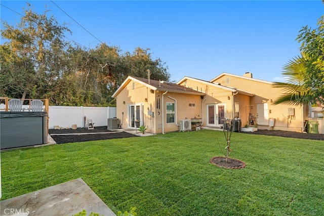 rear view of property with french doors, cooling unit, ac unit, a hot tub, and a lawn