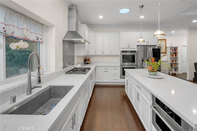 kitchen with pendant lighting, wall chimney range hood, sink, appliances with stainless steel finishes, and white cabinetry