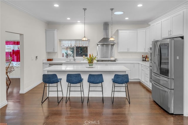 kitchen featuring a center island, white cabinets, wall chimney exhaust hood, appliances with stainless steel finishes, and decorative light fixtures