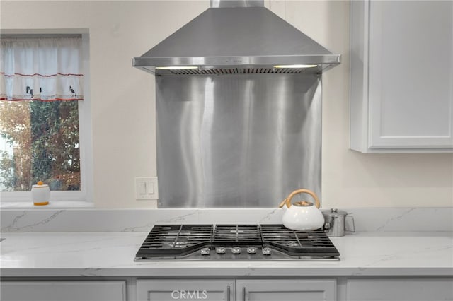 kitchen featuring white cabinetry, light stone counters, wall chimney exhaust hood, and stainless steel gas cooktop