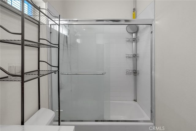 bathroom featuring toilet and combined bath / shower with glass door