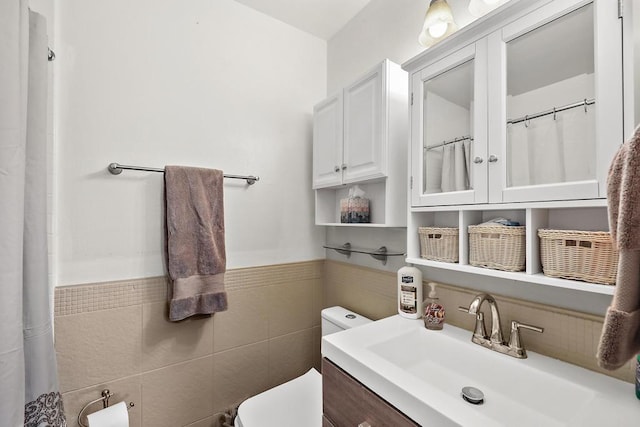 bathroom featuring vanity, toilet, and tile walls