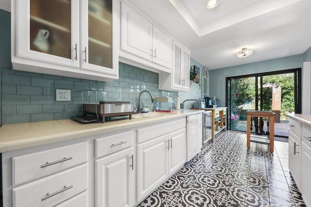 kitchen featuring dishwasher, white cabinets, a raised ceiling, sink, and tasteful backsplash