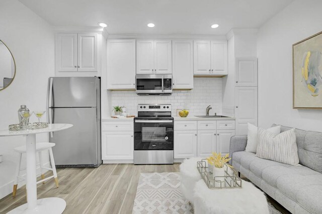 kitchen with stainless steel appliances, sink, white cabinets, light hardwood / wood-style flooring, and decorative backsplash