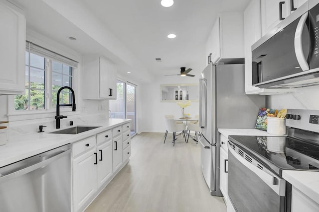 kitchen featuring stainless steel appliances, sink, white cabinetry, ceiling fan, and light wood-type flooring