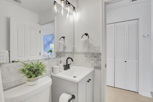 bathroom with toilet, vanity, and decorative backsplash