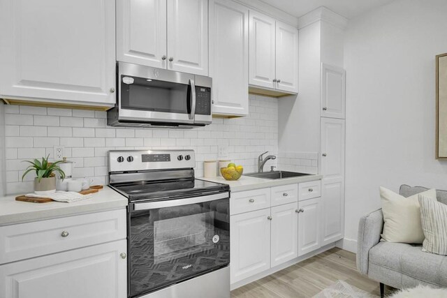 kitchen featuring appliances with stainless steel finishes, light wood-type flooring, sink, white cabinetry, and backsplash