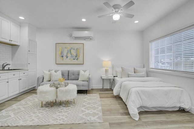 bedroom featuring ceiling fan, light wood-type flooring, sink, and a wall unit AC