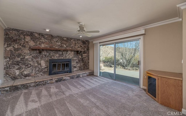 unfurnished living room with carpet flooring, ceiling fan, a stone fireplace, and ornamental molding