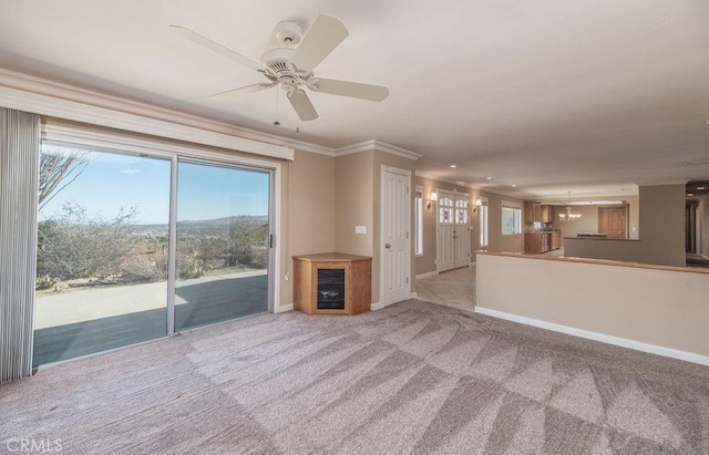 unfurnished living room with ceiling fan with notable chandelier, light colored carpet, and crown molding