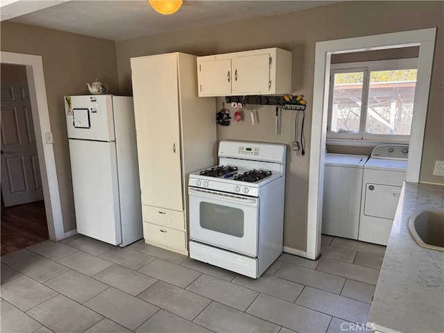 kitchen featuring white appliances, sink, light tile patterned floors, washing machine and clothes dryer, and white cabinetry