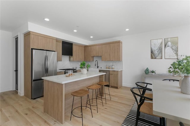 kitchen featuring appliances with stainless steel finishes, sink, backsplash, light hardwood / wood-style flooring, and a breakfast bar area