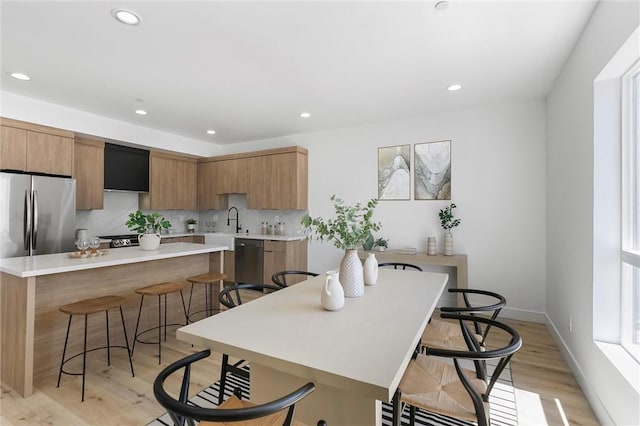 kitchen with sink, a kitchen bar, a kitchen island, light hardwood / wood-style floors, and stainless steel appliances