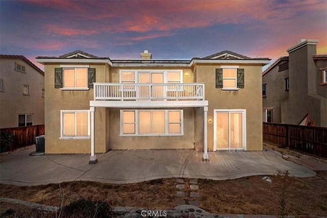 back house at dusk featuring a balcony, a patio, and central AC unit