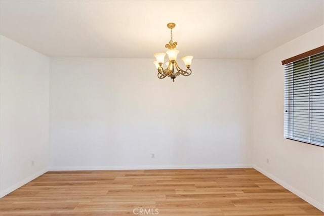 spare room featuring a chandelier and light hardwood / wood-style flooring