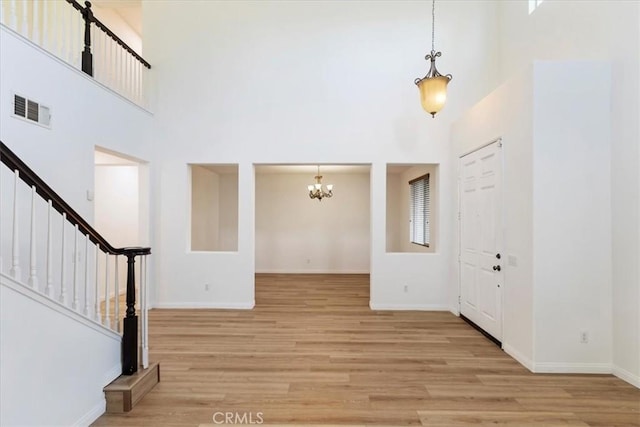 entrance foyer featuring light wood-type flooring, a towering ceiling, and an inviting chandelier