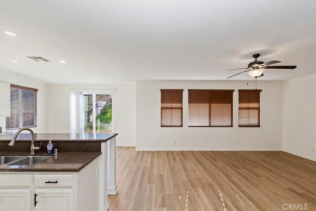 kitchen with ceiling fan, sink, dark stone counters, light hardwood / wood-style floors, and white cabinets