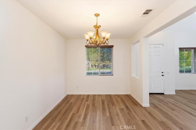 unfurnished room with a healthy amount of sunlight, a notable chandelier, and wood-type flooring