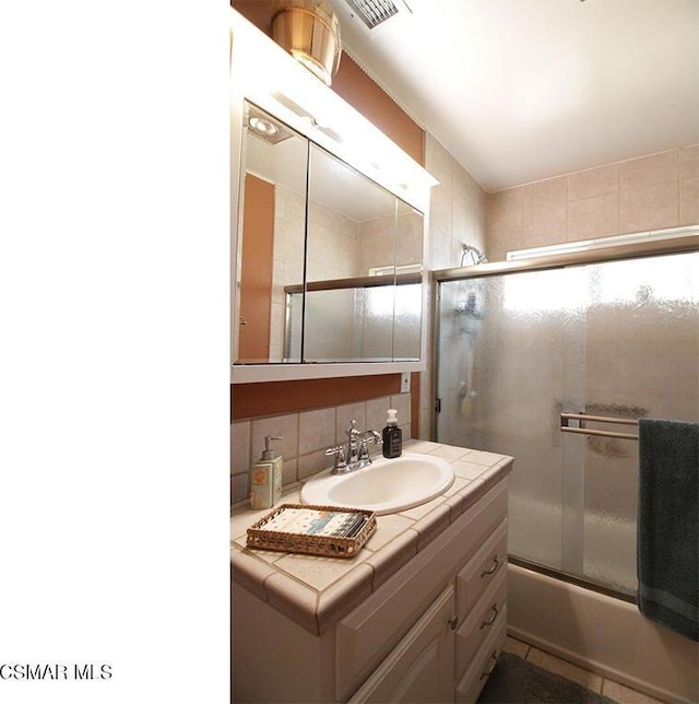 bathroom featuring backsplash, shower / bath combination with glass door, and vanity