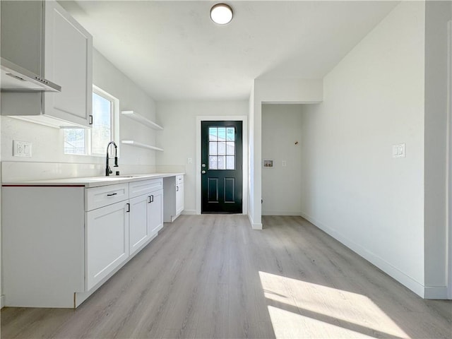 kitchen with white cabinets, light hardwood / wood-style flooring, wall chimney exhaust hood, and sink