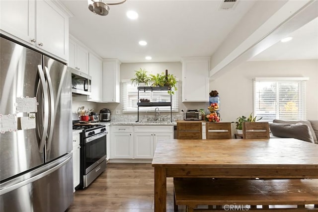 kitchen with sink, dark hardwood / wood-style floors, appliances with stainless steel finishes, light stone counters, and white cabinetry