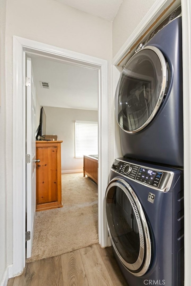 laundry area featuring stacked washer and dryer and light hardwood / wood-style flooring